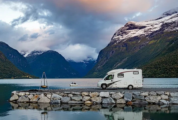 camper op pier meer en bergen in de achtergrond met bootje op het meer