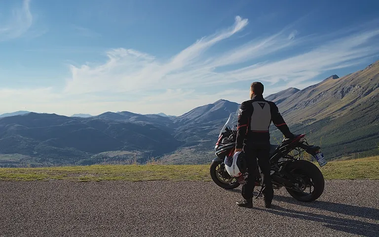 Motorrijder staand langs motor kijkend naar bergen in de achtergrond